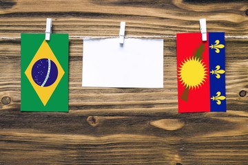 Hanging flags of Brazil and Guadeloupe attached to rope with clothes pins with copy space on white...