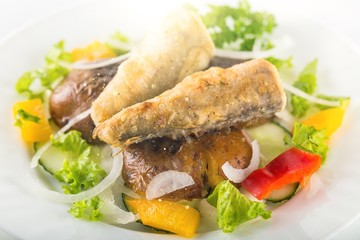 Fried fish in a salad on a white plate in the sun