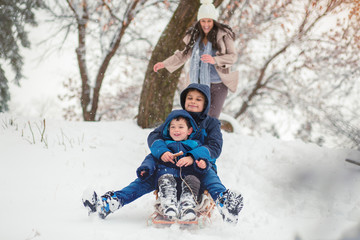 Fototapeta na wymiar Young mom chasing her cute sons while they are sledding