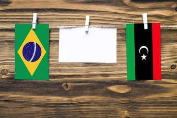 Hanging flags of Brazil and Libya attached to rope with clothes pins with copy space on white note paper on wooden background.Diplomatic relations between countries.