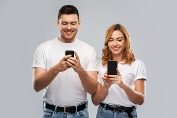 technology and people concept - happy couple in white t-shirts with smartphones over grey background