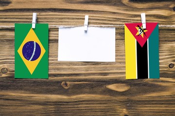 Hanging flags of Brazil and Mozambique attached to rope with clothes pins with copy space on white...