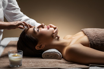 wellness, beauty and relaxation concept - beautiful young woman lying with closed eyes and having face and head massage at spa
