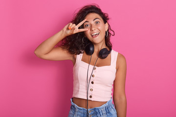 Close up portrait of young woman making victory or peace sign and covering her eye with it, posing...