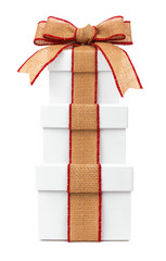 Stacked white Christmas gift boxes wrapped with rustic burlap bow and ribbon, isolated on a white...