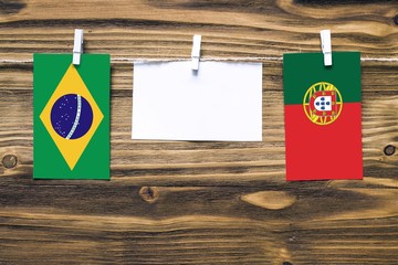 Hanging flags of Brazil and Portugal attached to rope with clothes pins with copy space on white note paper on wooden background.Diplomatic relations between countries.