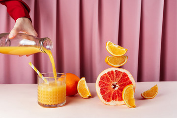 Woman pouring orange juice into the cup with ice on the table with various citrus fruits, selective...