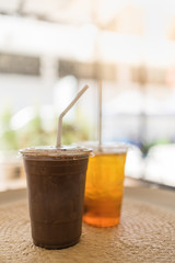 Close up of take away plastic cup of iced chocolate and iced tea on round table with copy space.