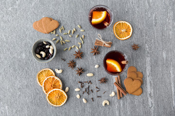 christmas and seasonal drinks concept - hot mulled wine, dry orange slices, raisins with cashew nuts and aromatic spices on grey background