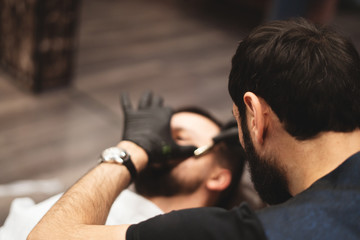 Shaving a beard in a barbershop with a dangerous razor. Barber Shop Beard Care. Drying, cutting, cutting a beard. Selective focus.