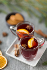 christmas and seasonal drinks concept - hot mulled wine, dry orange slices, gingerbread and aromatic spices on grey background