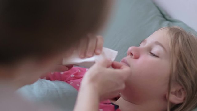 Mother is giving digital thermometer to her cold little daughter, lying on a couch in home