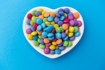 sweets, confectionery and valentine's day concept - candy drops on heart shaped plate over blue background