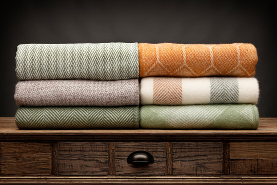 6 luxury throws, folded up and shot on a wooden sideboard,  with a grey background