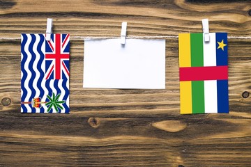 Hanging flags of British Indian Ocean Territory and Central African Republic attached to rope with clothes pins with copy space on white note paper on wooden background.