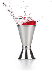 red liquid spilling out of a jigger isolated on white