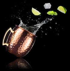mint, lime and ice cube falling out of a splashing moscow mule isolated on black