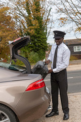 Andover, Hampshire, UK. October 2019.  A smartly dressed chauffeur, loading luggage into boot of a luxury car.