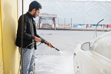 South asian man or indian male washing his white transportation on car wash.