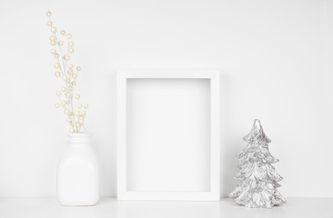 Mock up white frame with silver Christmas tree and branches on a shelf. Portrait frame against a white wall.