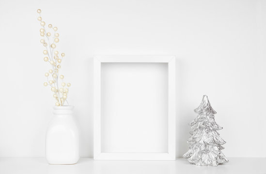 Mock up white frame with silver Christmas tree and branches on a shelf. Portrait frame against a white wall.