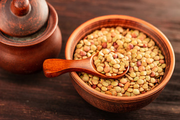 Lentils in a clay vessel on and wooden spoon on a wooden background