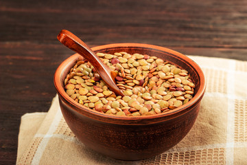 Lentils in a clay vessel and a wooden spoon on a napkin and wooden background