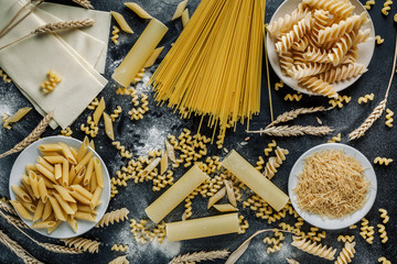 Different types of Italian pasta on a dark wooden rustic background. Mixed dry pasta and spaghetti. Still life. Rustic style. Top view.