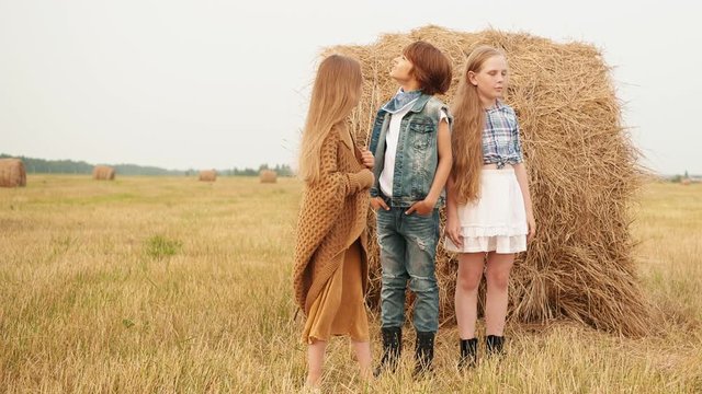 Three teenagers standing near haystack in field and looking at sky. Adorable teenage boy and girls standing near hay on autumn field and looking up