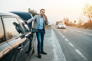 Elegant middle age business man calling towing service for help on the road. Roadside assistance...