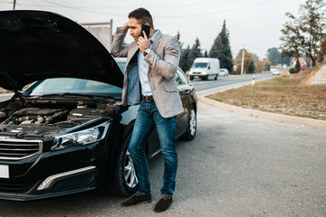 Elegant middle age business man calling towing service for help on the road. Roadside assistance...