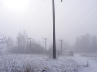 Voltage line. The poles on the field in misty weather. Power supply infrastructure during winter. Fog conditions with a little bit of snow.
