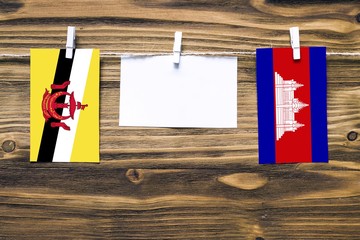 Hanging flags of Brunei and Cambodia attached to rope with clothes pins with copy space on white...