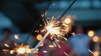 Sparklers close up, orange lights fall on all sides. Bright burning wand of bengal light, spark super slow motion. Christmas, New Year celebration
