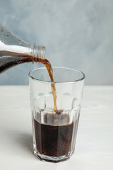 Pouring refreshing soda drink into glass on white wooden table against blue background