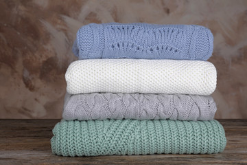 Stack of folded knitted sweaters on wooden table against brown background