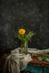 Beautiful fresh summer still life with a bouquet of yellow dandelions in a pot of red clay. Still life in a rustic style against a dark background. The concept of rural life. Selective focus.