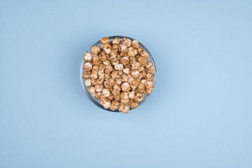 Caramel sweet popcorn glass bowl isolated on blue background top view. Top view, copy space.