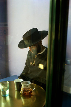 Man wearing a black wide brim hat and crucifix sitting in caf?