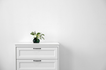 Modern chest of drawers with fresh flowers near wall. Space for text