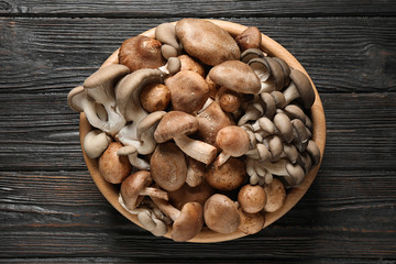 Different fresh wild mushrooms in bowl on wooden background, top view