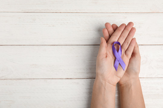 Woman holding purple ribbon on white wooden background, top view with space for text. Domestic violence awareness