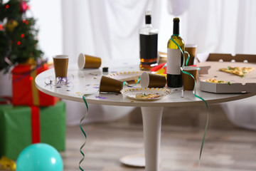 Messy table with cups, bottles and pizza indoors. Chaos after party