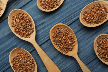 Buckwheat grains in spoons on blue wooden table, flat lay
