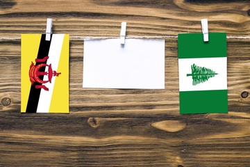 Hanging flags of Brunei and Norfolk Island attached to rope with clothes pins with copy space on white note paper on wooden background.Diplomatic relations between countries.