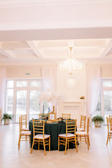 Table decoration with flowers in white colors. Elegant dining table in green-golden color. Indoors wedding. Devices and chairs in golden colors. Beautiful table setting, tablecloth green.