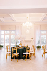 Table decoration with flowers in white colors. Elegant dining table in green-golden color. Indoors wedding. Devices and chairs in golden colors. Beautiful table setting, tablecloth green.