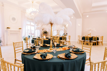 Table decoration with flowers in white colors. Elegant dining table in green-golden color. Indoors wedding. Devices and chairs in golden colors. Beautiful table setting, tablecloth green.