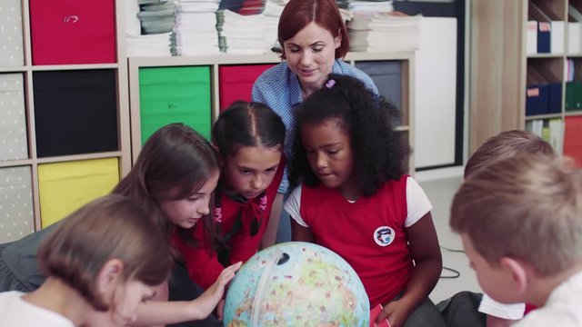 A group of small school kids with teacher sitting on the floor in class, learning.