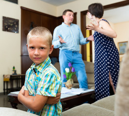 Unhappy small boy sitting  at sofa during his parents quarrelling
